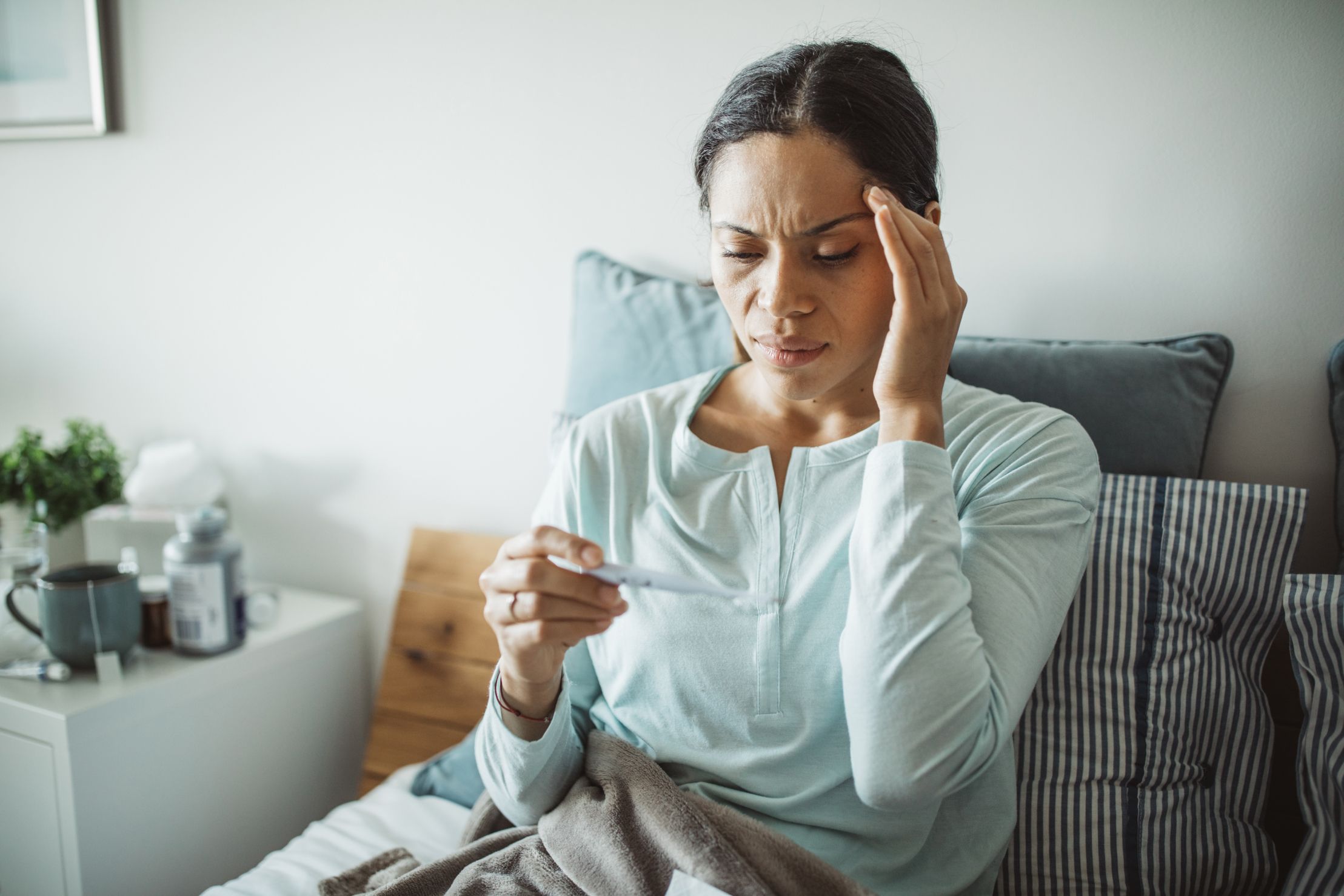 woman with headache feeling sick taking her temperature wonders if she has been exposed to covid-19