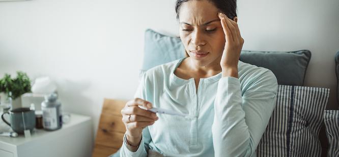 woman with headache feeling sick taking her temperature wonders if she has been exposed to covid-19