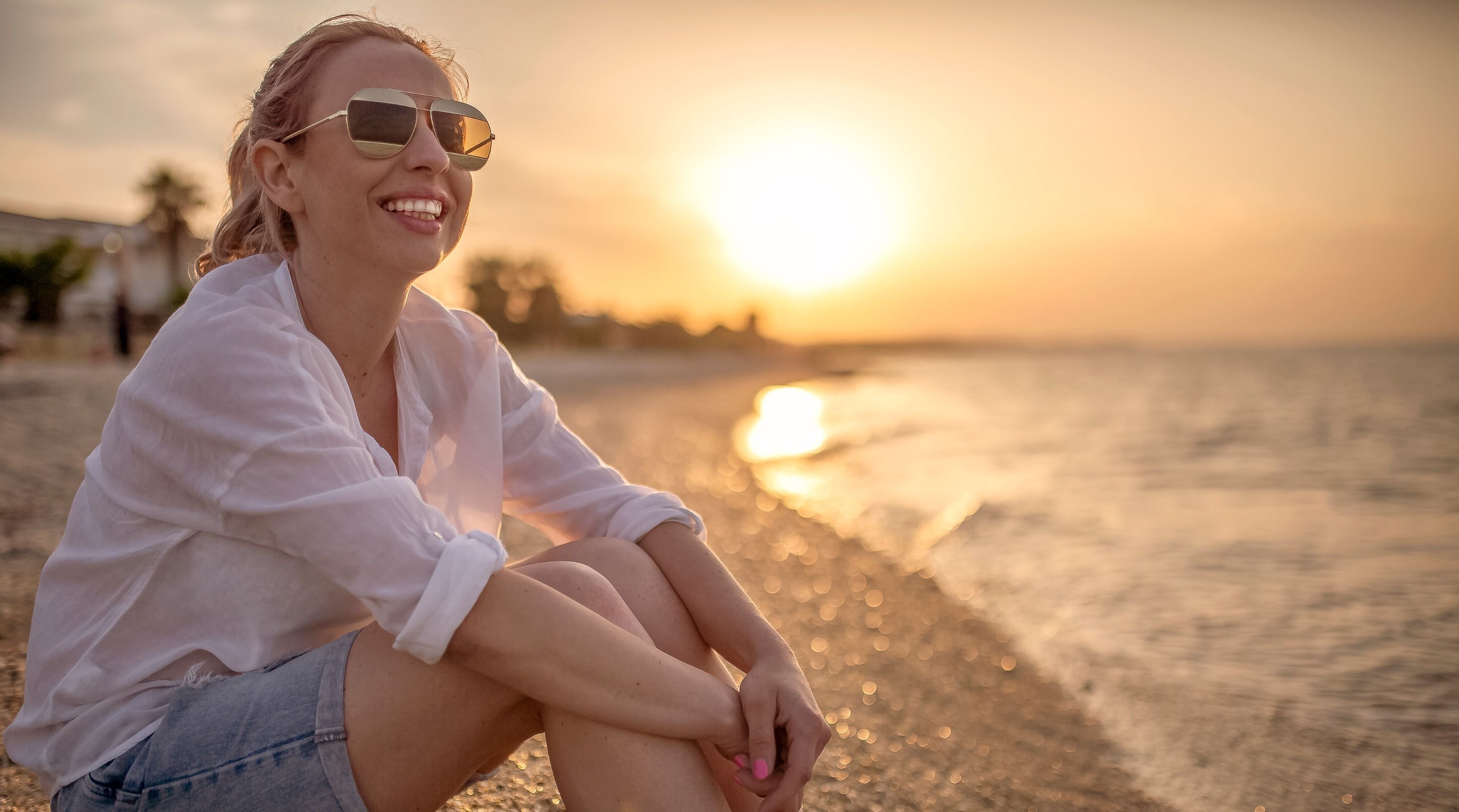 woman wearing sunglasses at the beach and sunscreen following dermatologist advice
