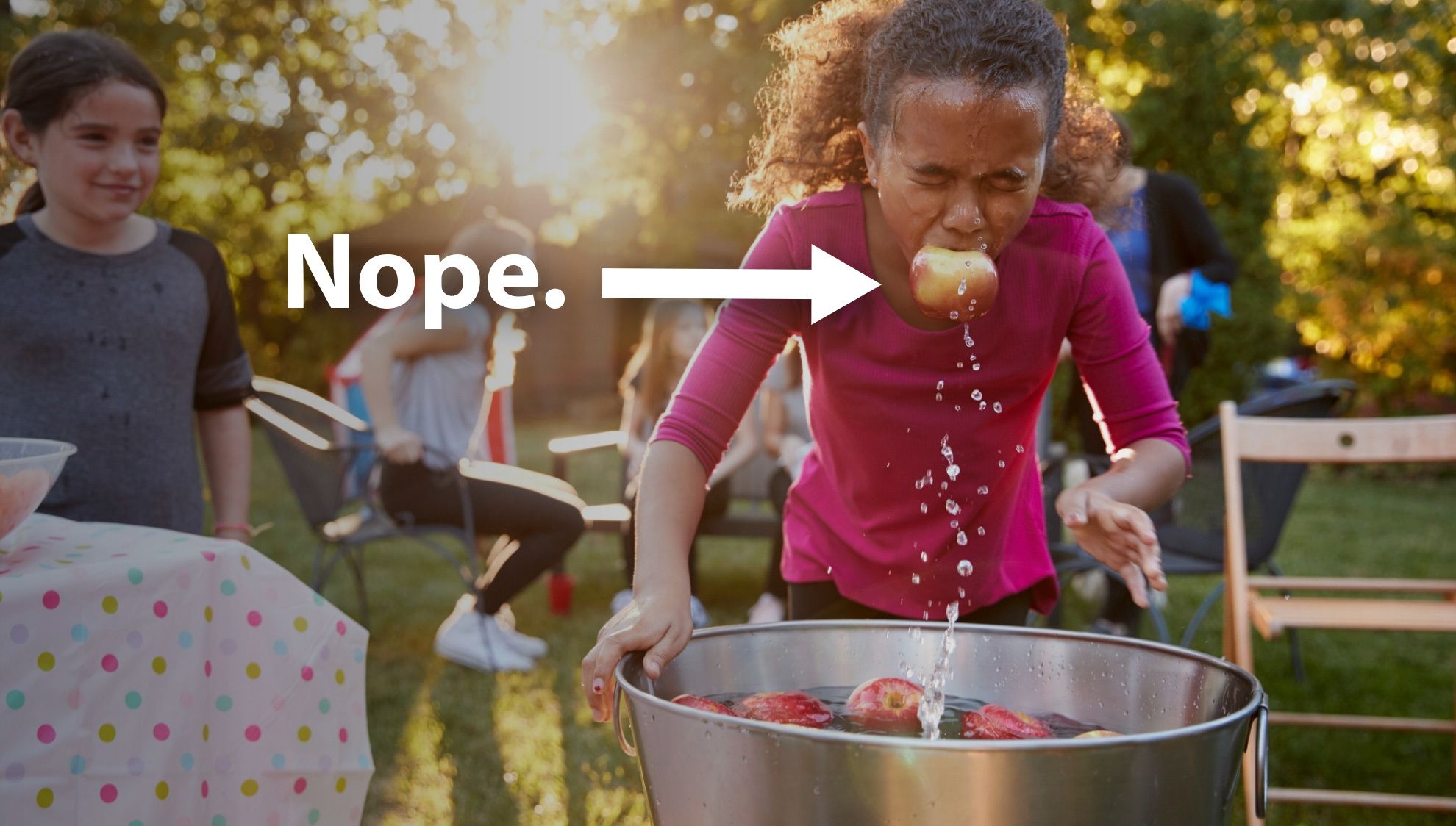 girl in pink shirt bobbing for apples outside at party