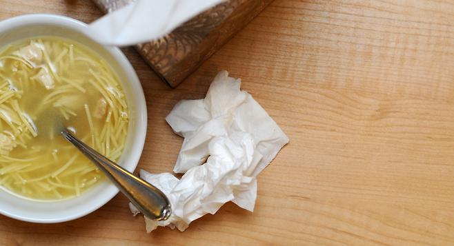 bowl of chicken noodle soup with kleenex for someone sick with covid-19