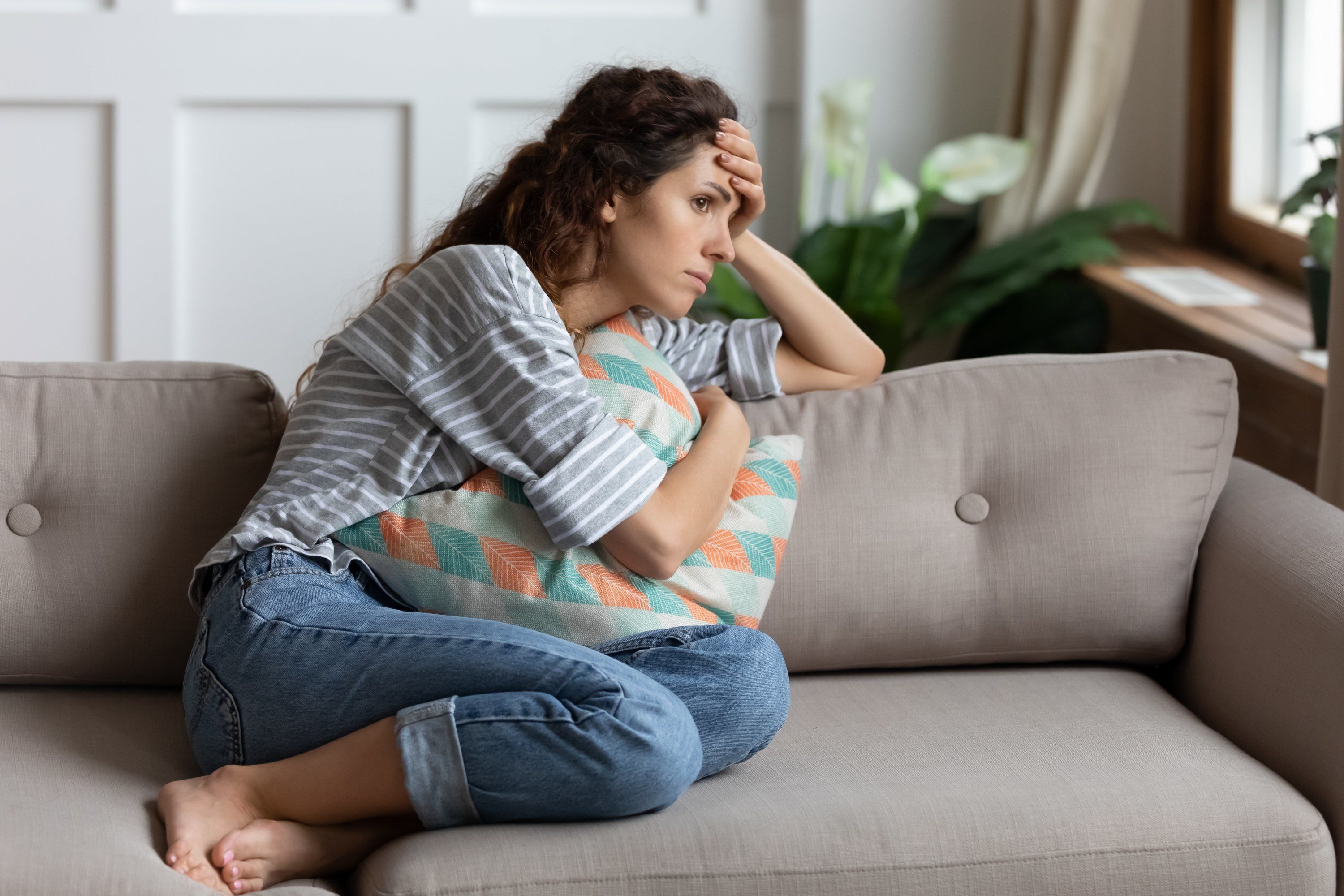 woman sitting on the couch feeling stressed and sick and needs to see primary care doctor