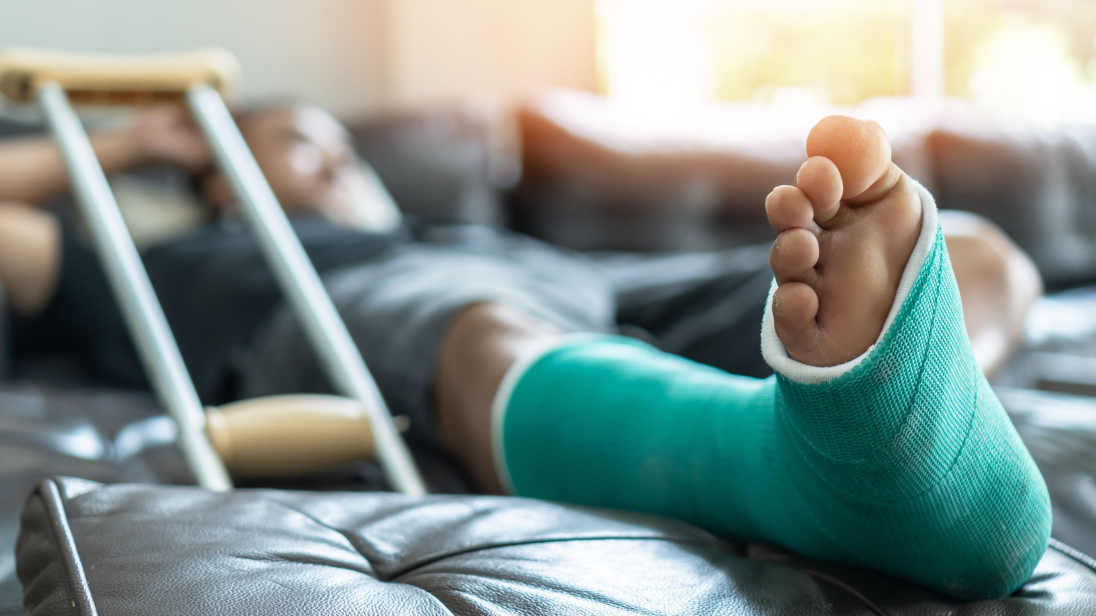 man reclining on couch with green cast on broken foot after going to urgent care