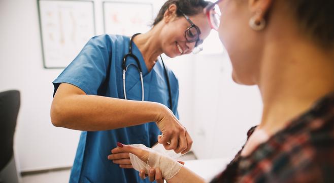 woman receiving wound care from smiling nurse at urgent care stitches and bandage