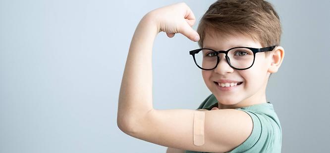 Child wearing glasses showing arm after vaccine