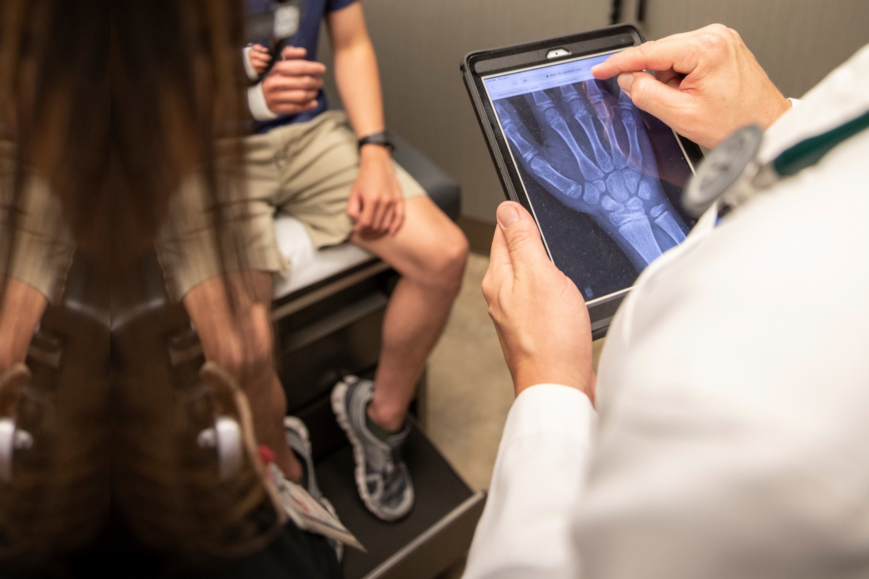 doctor reading digital hand xray on ipad while patient sits on exam table with arm cast